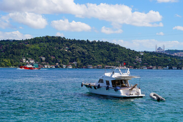 Obraz premium Luxury yacht sailing on the serene Bosphorus with lush green hills and an Istanbul mosque in the backdrop