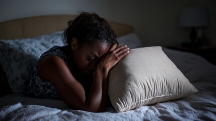 A woman suffering from insomnia covers her head with a cushion to block out the light, seeking relief from her sleeplessness. She clutches a pillow tightly