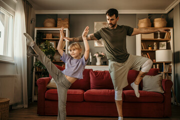 Cheerful dad and daughter having fun while practicing yoga and pilates at home.