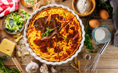 Top view of a freshly baked savory quiche with a flaky crust, filled with eggs, bacon, and cheese, set on a wooden background