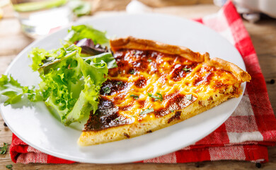 Top view of a slice of Quiche Lorraine with salad on a plate and a fork – a savory French dish with eggs, bacon, and cheese, served with a fresh, healthy side salad.