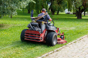 A person operating a lawn mower in a park, cutting the grass. The person is wearing a hat and headphones, focused on the task at hand