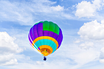 Colorful hot air balloon flying over blue sky with white clouds