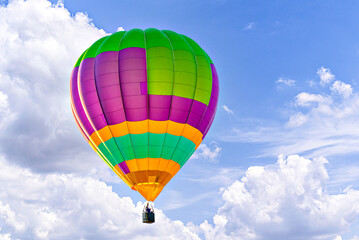 Colorful hot air balloon flying over blue sky with white clouds