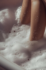 Close-up of legs relaxing in a foamy bath with bubbles and soft textures