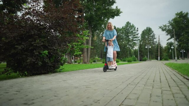 A mother and son riding a scooter down a smooth, interlocked walkway in a peaceful park