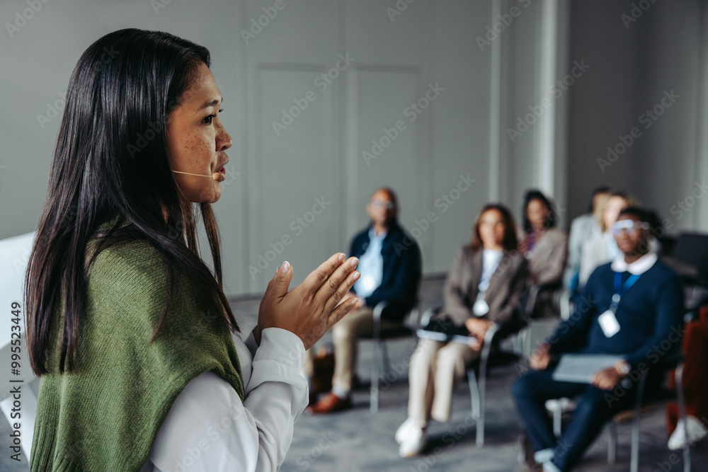 Wall mural Confident female speaker leading a seminar with an engaged audience in a professional conference setting