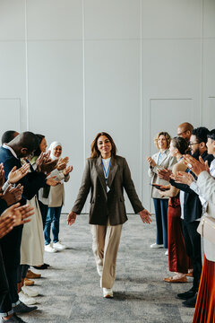 Successful female leader walking between supportive colleagues clapping in appreciation at a business meeting in a modern office setting.