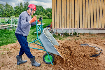 Construction worker fills area around septic tank manhole cover with sand using wheelbarrow.