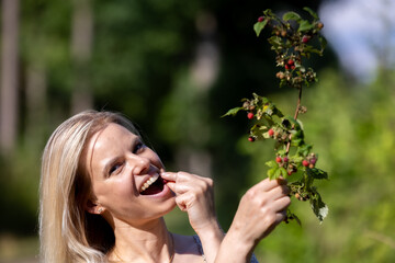 Young beautiful woman eating wild raspberries in the forest