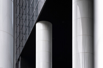 Polished white pillars stand tall as structural elements under a modern architectural design, offering a clean and sleek contrast against darker elements in the background.