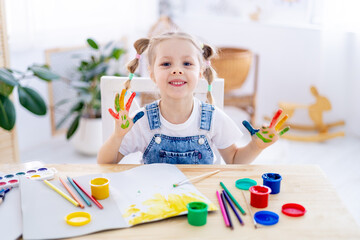 portrait of a small child girl with stained multicolored hands in finger gouache or in paint,...