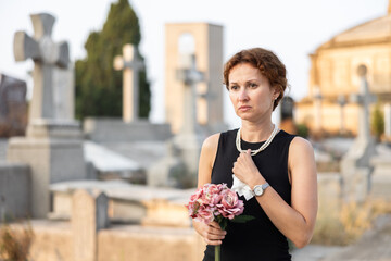 Visit to cemetery, woman in mourning clothes grieves for deceased relative. Near grave widow...