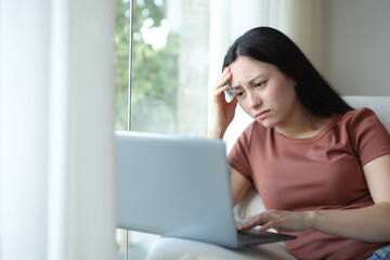 Worried asian woman checking laptop at home