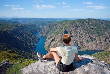person sitting on a rock in the mountains looking at the view of the river canyon