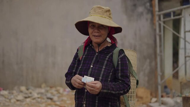 mature vietnamese woman with a big hat on her head counts the money she has in her hands after a payment
