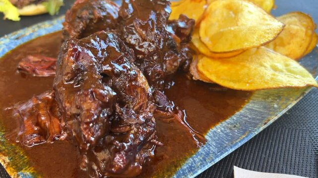 Traditional Spanish oxtail stew with homemade potato chips, tender slow cooked meat in red wine sauce in Malaga Spain, delicious food, 4K shot