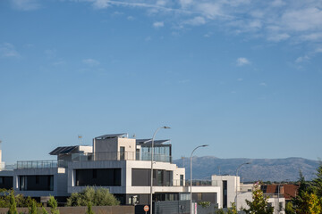 It dawns in an urbanization of individual chalets with modern architecture. They have photovoltaic solar panels on the roofs, the sky is clear and blue. Sustainability and sustainable urbanism