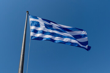 Greek flag waving on flagpole with blue sky in background