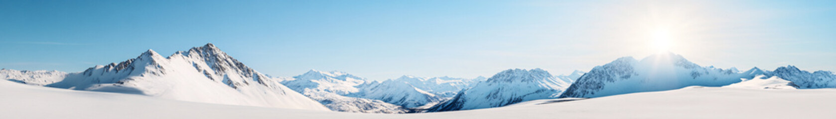 A sweeping panoramic view of a snow-covered mountain range, with jagged peaks piercing through the cloudless sky. The snow glistens under the midday sun, casting long shadows across the slopes. The