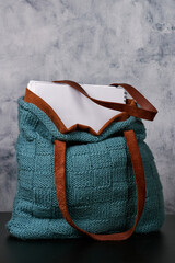 A cozy blue knitted bag with brown handles and a notebook inside
