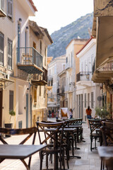 Nestled in Nafplio, cozy cafes line the sunlit alley, inviting visitors to unwind. Lively conversations and aromatic coffee fill the air as people enjoy the vibrant atmosphere.