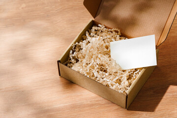 Open cardboard box filled with shredded paper and a blank card on a wooden surface