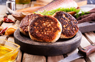Cooked fried fish cutlets in a plate, on a light wooden table.