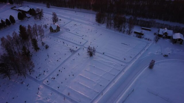 Aerial view during winter in north of Sweden, flying over a road with cars and fields covered in snow slowly tilting up revealing a frozen lake and the sun setting behind the mountains