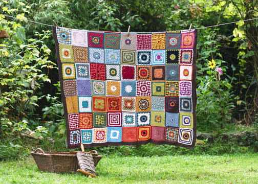 Vintage colorful blanket, make from crochet granny squares with different motifs, hangs on the string in the summer cottage garden. Copy space. Hobby and handmade concept.