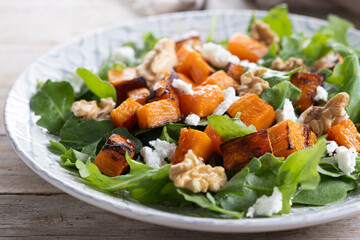 Pumpkin salad with arugula, walnuts and feta cheese on wooden table. Autumn healthy food