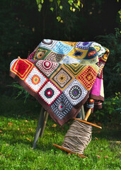 Beautiful multi colored crocheted plaid made from woolen granny squares lies on a rustic chair close by an antique wooden clothespin with rope. Copy space.