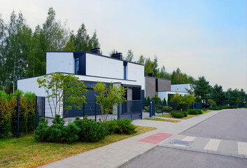 Obraz premium Prefab house. Street in residential area. Contemporary Residence in suburb. Rows of modern houses along road. Family house, Modern Home outside city. Trees, green lawn at Modern Villa.