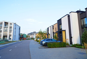 Obraz premium Modern townhouses in residential area. New apartment buildings in green in enviroment. Street with Townhouse along sidewalk with green lawn. Car on parking lot at house. Townhouse in suburb.