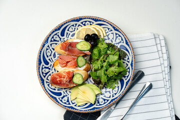 Colorful plate of smoked salmon sandwiches with cucumbers, greens, and olives on a decorative blue platter