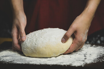 Woman's hands holding dough over kitchen board, warm photo of home baking process.	