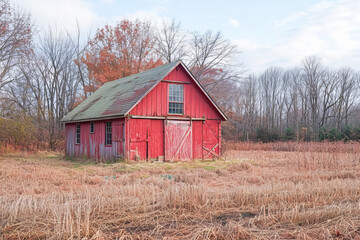 Obraz premium Old red barn standing in fallow field on winter day