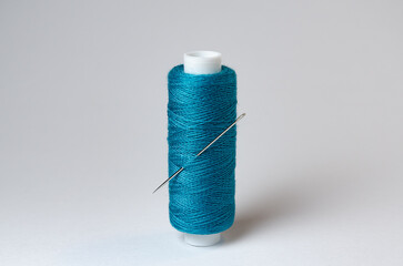 One single turquoise thread spool with needle on white background