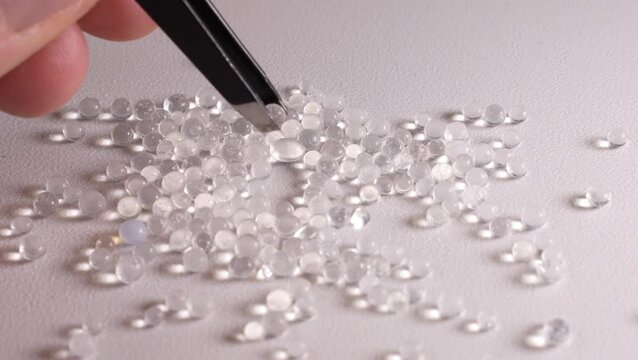 Close-up view of transparent and opaque plastic pellets being examined with tweezers, representing the environmental issue of microplastic pollution in water bodies and the importance of legislation
