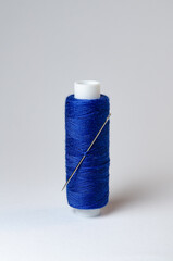 One single dark blue thread spool with needle on white background