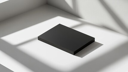 A minimalist black rectangular object on a light surface with shadows.