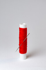 One single red thread spool with needle on white background
