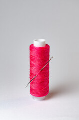 One single pink thread spool with needle on white background