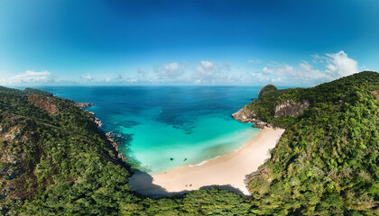 Aerial view of vibrant turquoise waters nestled between steep rocky cliffs, greenery and sandy beach