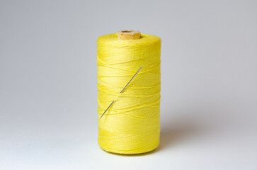 One single yellow thread spool with needle on white background