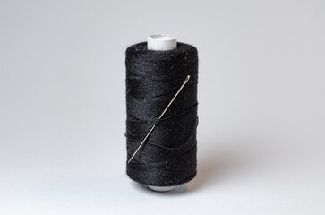 One single black thread spool with needle on white background