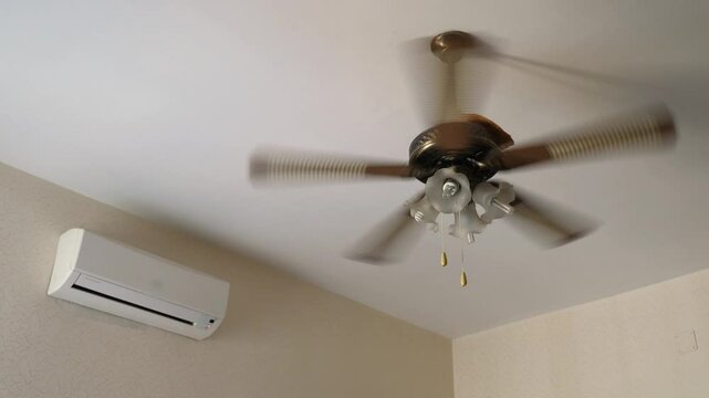 A ceiling fan and air conditioner are both running to cool the room, highlighting the struggle with extreme heat and climate change.