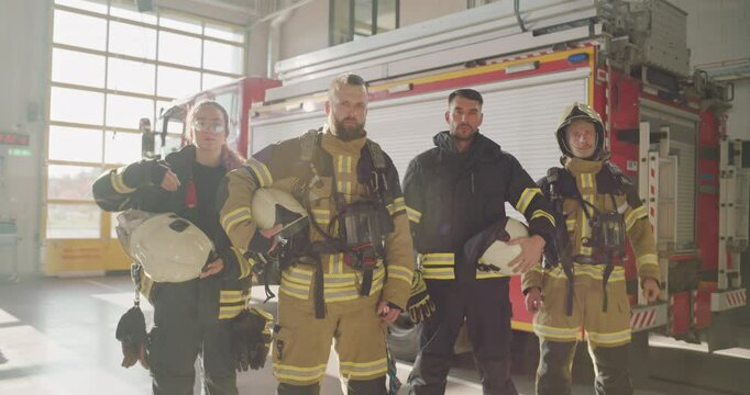 Four Firefighters, Three Men and One Woman, Standing Together in Full Gear, Posing for a Portrait in the Fire Station Garage. Fire Truck in the Background Completes the Scene