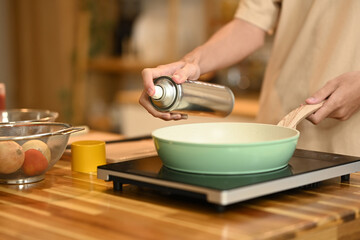 Close up woman spraying cooking oil onto frying pan on stove