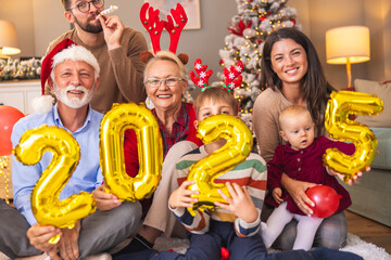 Happy family holding balloons shaped as numbers 2025 while having New Year party